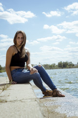 Chica adolescente posando en el embarcadero. Adolescente rubia de quince años como modelo. Chica rubia de pelo largo al lado del rio en verano. 
