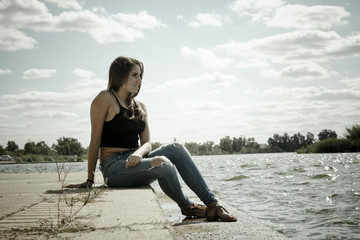 Fototapeta na wymiar Chica adolescente posando en el embarcadero. Adolescente rubia de quince años como modelo. Chica rubia de pelo largo al lado del rio en verano. 