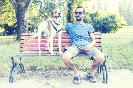 Young Man With His Dog Sitting On A Park Bench