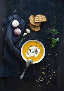Pumpkin soup with cream, seeds, bread and fresh basil on grunge