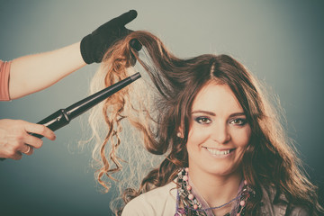 Hairdresser curling woman hair with iron curler.