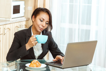 Businesswoman with cup of coffe using laptop in kitchen