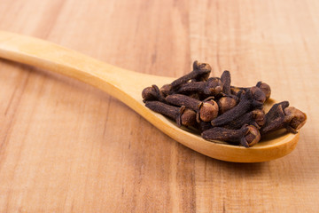 Heap of cloves with wooden spoon on table, seasoning for cooking