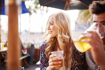 woman with her boyfriend enjoying drinking a beer at outdoor beach side bar or pub - obrazy, fototapety, plakaty