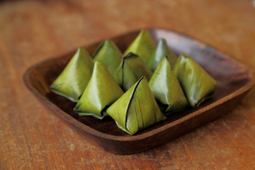 Thai dessert wrapped in banana leaves on wooden dish.