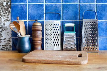 Different kinds stainless steel grater, green jug,  spoons, cutting board.