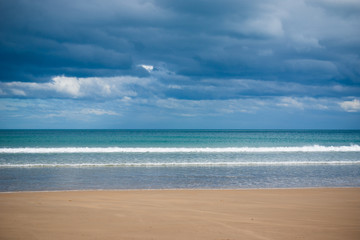 Small waves break on a sandy beach on a stormy day
