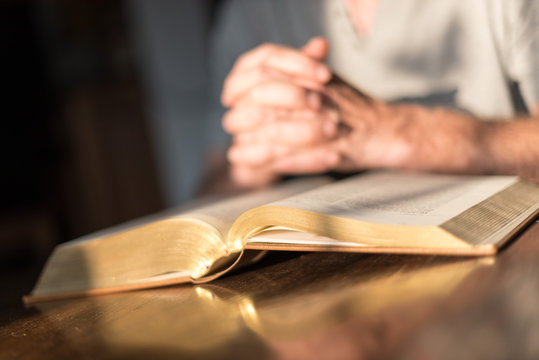 Man praying hands on a Bible