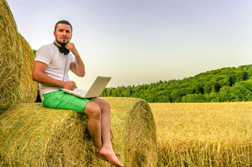 Naklejka na ściany i meble Country man with a laptop sitting on the hay.