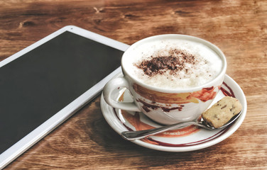 Cup of hot cappuccino and tablet.