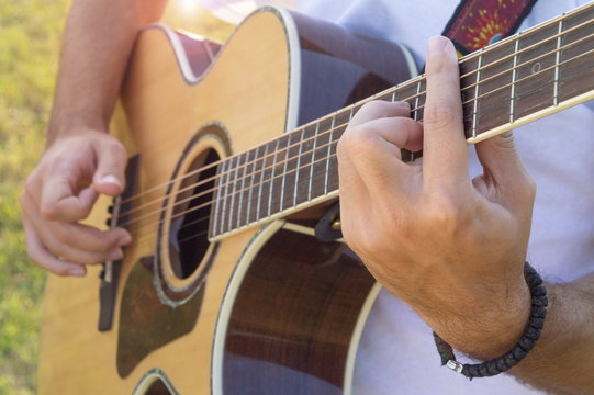 Man's hands playing acoustic guitar outdoors