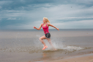 Blond female in sportswear running near the sea over blue sky wi