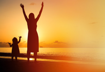 silhouette of mother and little daughter hands up at beach