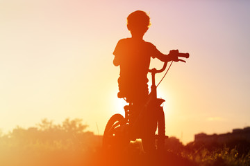 Obraz na płótnie Canvas little boy riding bike at sunset