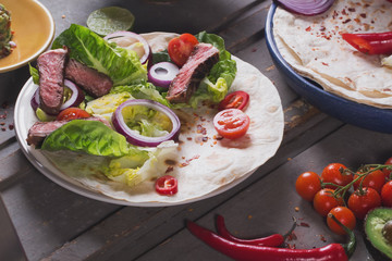Mexican tortillas with green fresh salad filling, beef, onions, tomatoes with gucamole and tortilla chips on te vintage board