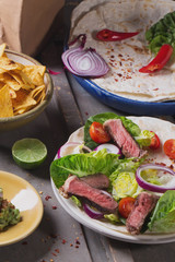 Mexican tortillas with green fresh salad filling, beef, onions, tomatoes with gucamole and tortilla chips on te vintage board