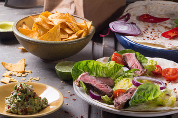 Mexican tortillas with green fresh salad filling, beef, onions, tomatoes with gucamole and tortilla chips on te vintage board