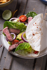 Mexican tortillas with green fresh salad filling, beef, onions, tomatoes with gucamole and tortilla chips on te vintage board