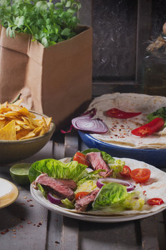 Mexican tortillas with green fresh salad filling, beef, onions, tomatoes with gucamole and tortilla chips on te vintage board