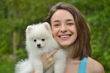 Attractive young woman holding german spitz puppy outside and smiling at camera.