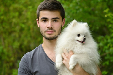 Attractive young man holding german spitz puppy outside and looking at camera.