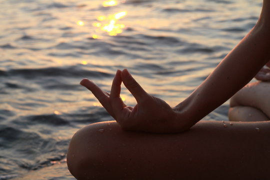 Clope up on women hands meditating in yoga position on the beach near the sea at sunset
