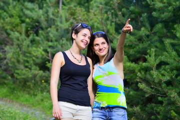 Fototapeta na wymiar Two beautiful girls walking on a path in the forest. One pointing to the other.