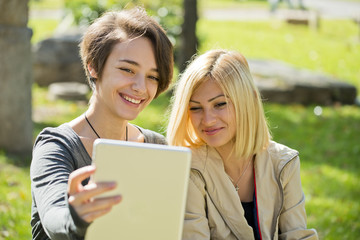 Two beautiful young women browsing tablet outside.