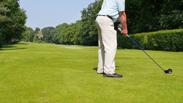 A man is playing a drive at a golf course on a warm sunny day. The camera is behind the player.