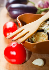 vegetables/ wooden fork, fried eggplant with garlic in a ceramic bowl and raw cloves of garlic, tomatoes and eggplant, selective focus