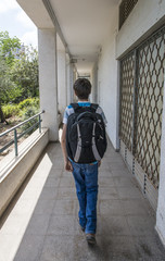 Teenage school boy with a backpack on his back walking to school. back view