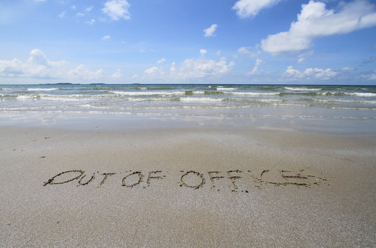 Out of office handwritten in sand on a beach