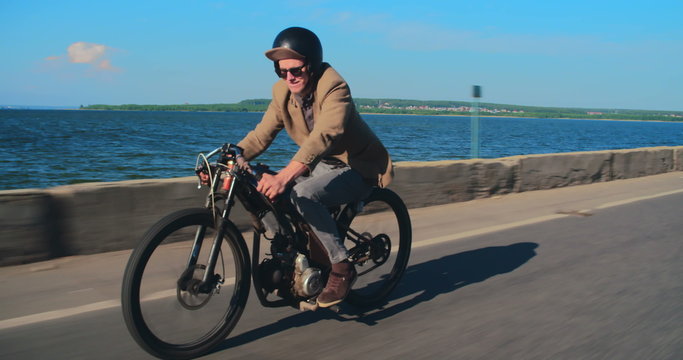 Young hipster enjoying ride on retro motorbike down road along sea