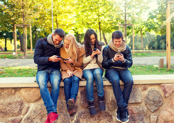 smiling friends with smartphones in city park