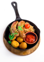 Grilled pork sausages with potato and red sauce in the bowl served in the pan on the wooden plate
