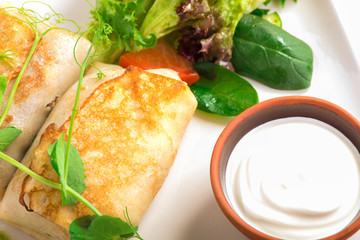 pancakes with forced meat green fresh salad and sour cream on the white plate