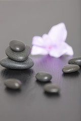 Fototapeta na wymiar Pile of three spa stones with a purple Orchid flower head