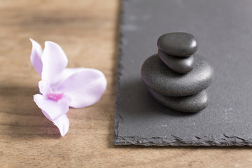 Fototapeta na wymiar Pile of four spa stones with a fresh orchid flower next to it on a slate tray