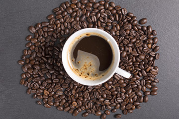 Still life of fresh roasted coffee beans with a white mug on a black slate surface