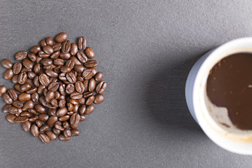 Still life of fresh roasted coffee beans with a white mug on a black slate surface