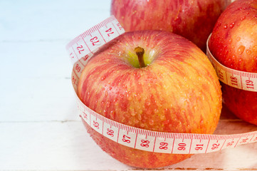 Fresh apples with measure tape on white wood background