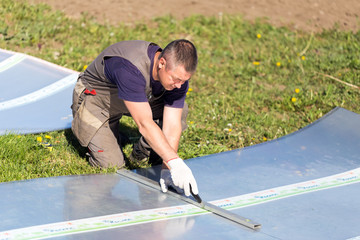 Worker in overalls with a knife cuts the polycarbonate sheet