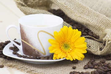 cup of coffee with yellow gerbera and coffee beans