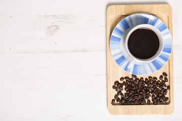 Fresh cup of coffee with roasted beans scattered around on a serving tray