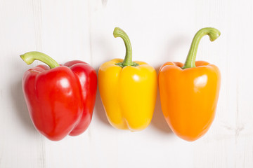 Three fresh red yellow and orange peppers on a light wooden kitchen surface