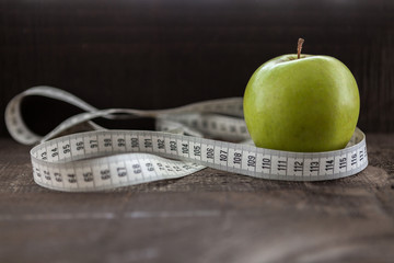  apple surrounded by a measuring tape referring to diet and health concept on wooden background