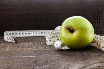  apple surrounded by a measuring tape referring to diet and health concept on wooden background