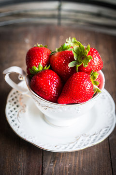 Fresh strawberries in a cup on wooden background