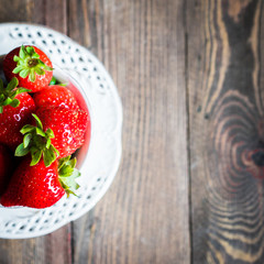 Fresh strawberries in a cup on wooden background