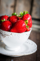 Fresh strawberries in a cup on wooden background